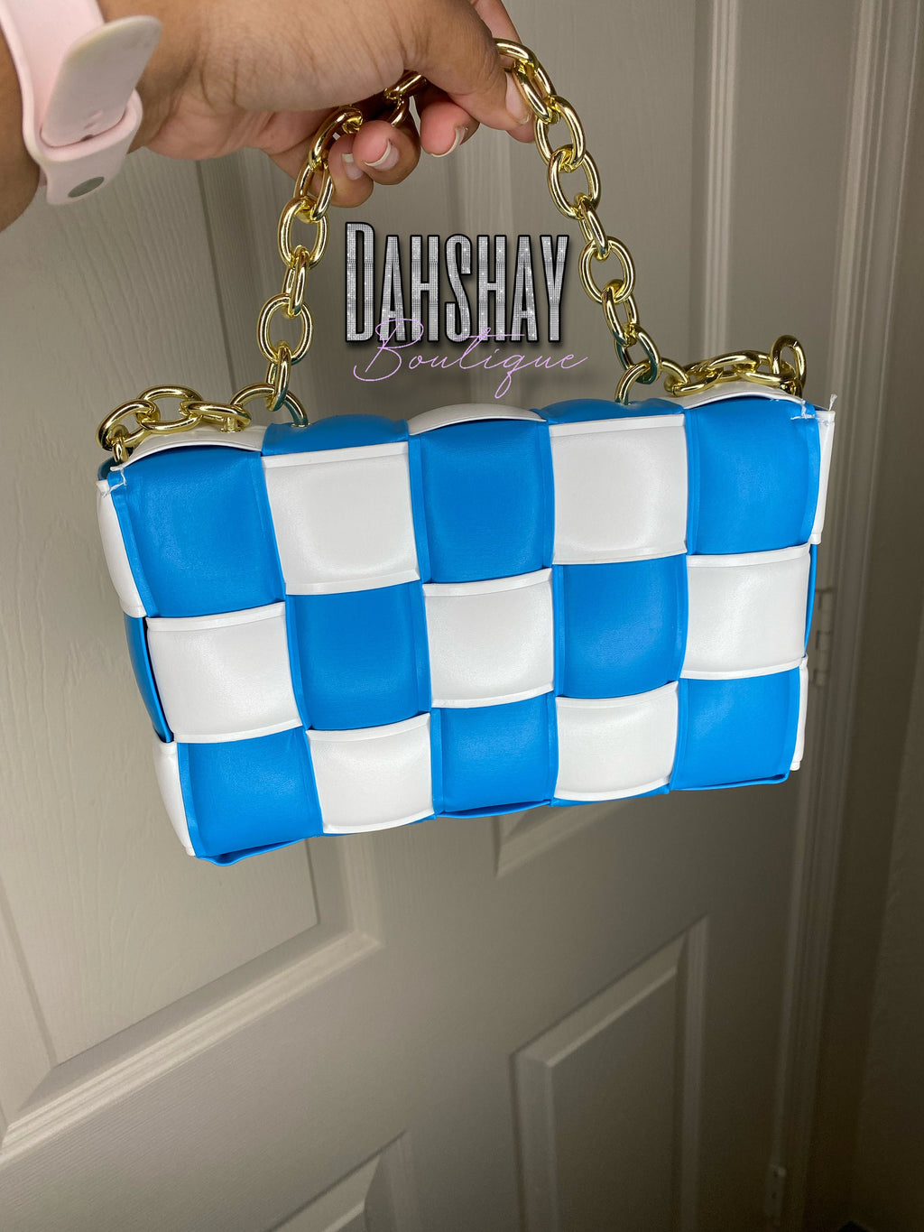 Blue and white checkered handbag with gold chain handle held by a person, against a neutral background.