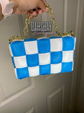 Blue and white checkered handbag with gold chain handle held by a person, against a neutral background.