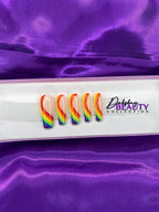 Rainbow-colored press-on nails on a white tray with 'Dahshay Beauty Collection' branding against a purple satin background.