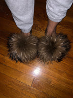 Fuzzy slippers worn on a wooden floor with gray sweatpants.