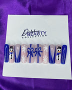 Press On Nails with Christmas designs of snowmen, bows  and a snowflake on a white card against a purple satin background.