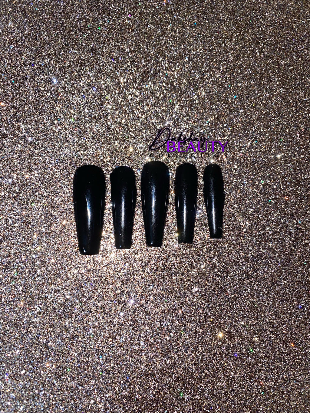 Set of black nail tips on a glittery gold background.