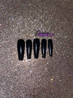 Set of black nail tips on a glittery gold background.