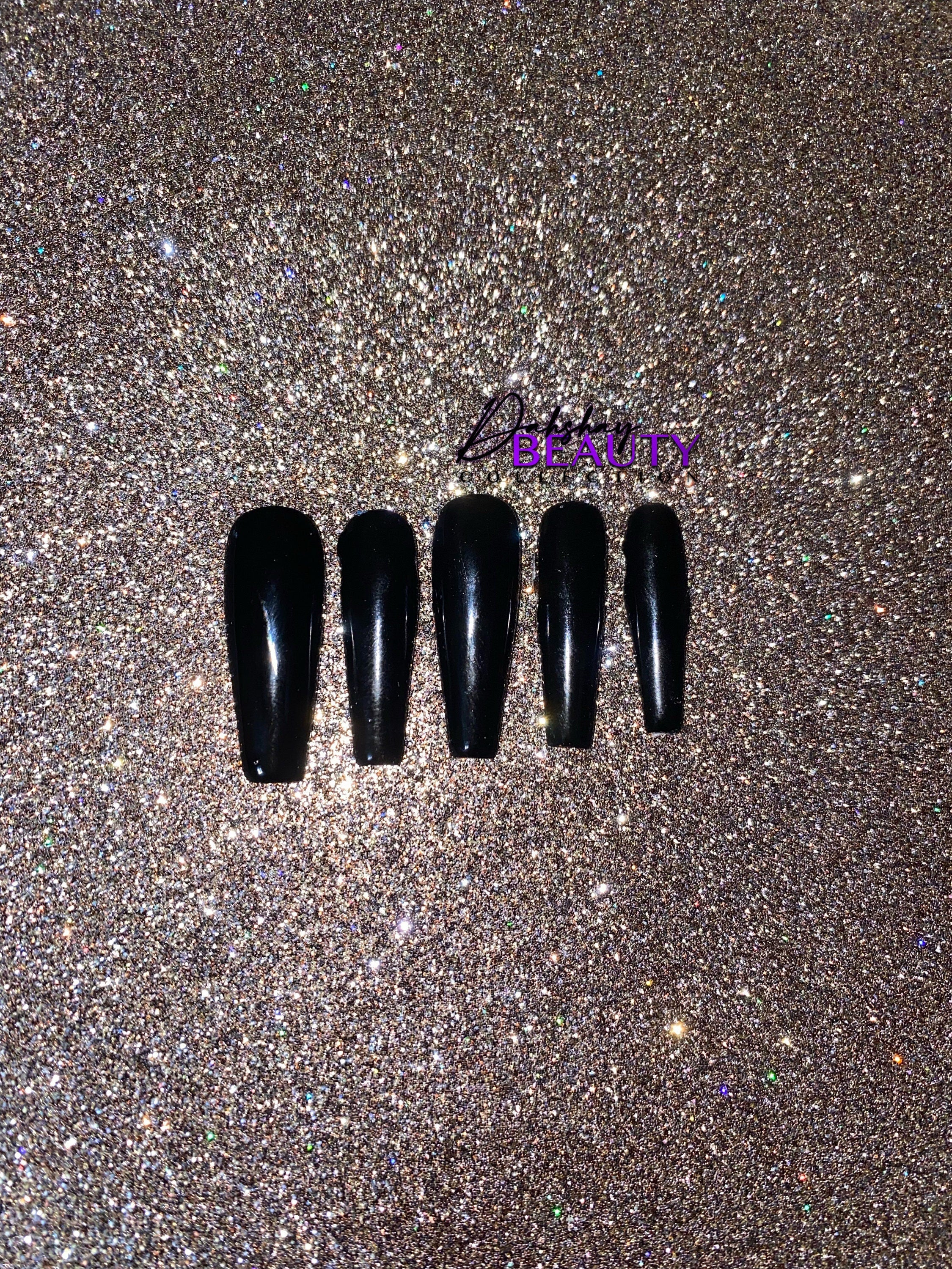 Set of black nail tips on a glittery gold background.