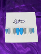 Set of blue, grey and white nails on while paper with a purple satin background.