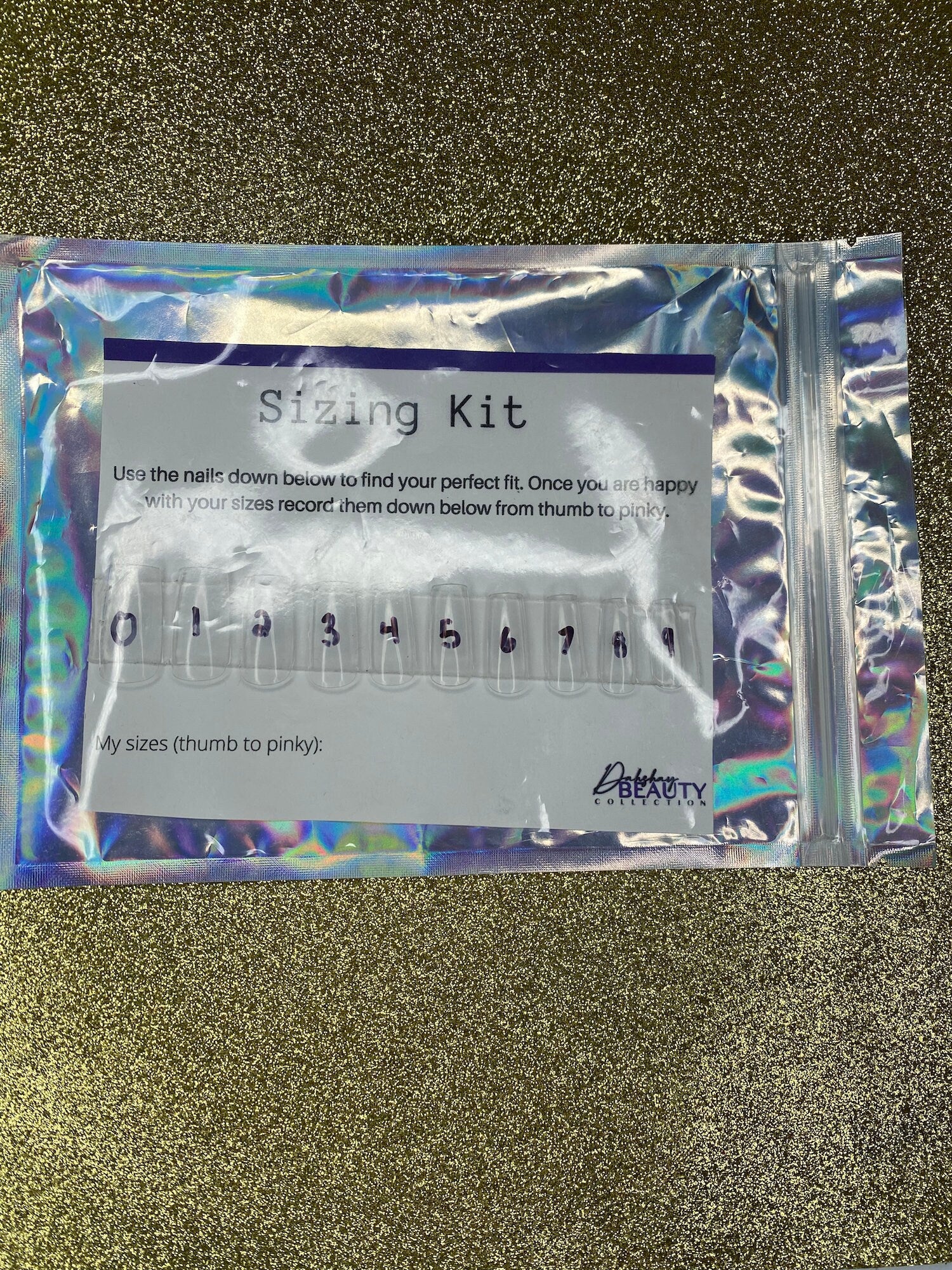 Sizing kit for false nails in a clear plastic package on a glittery black background