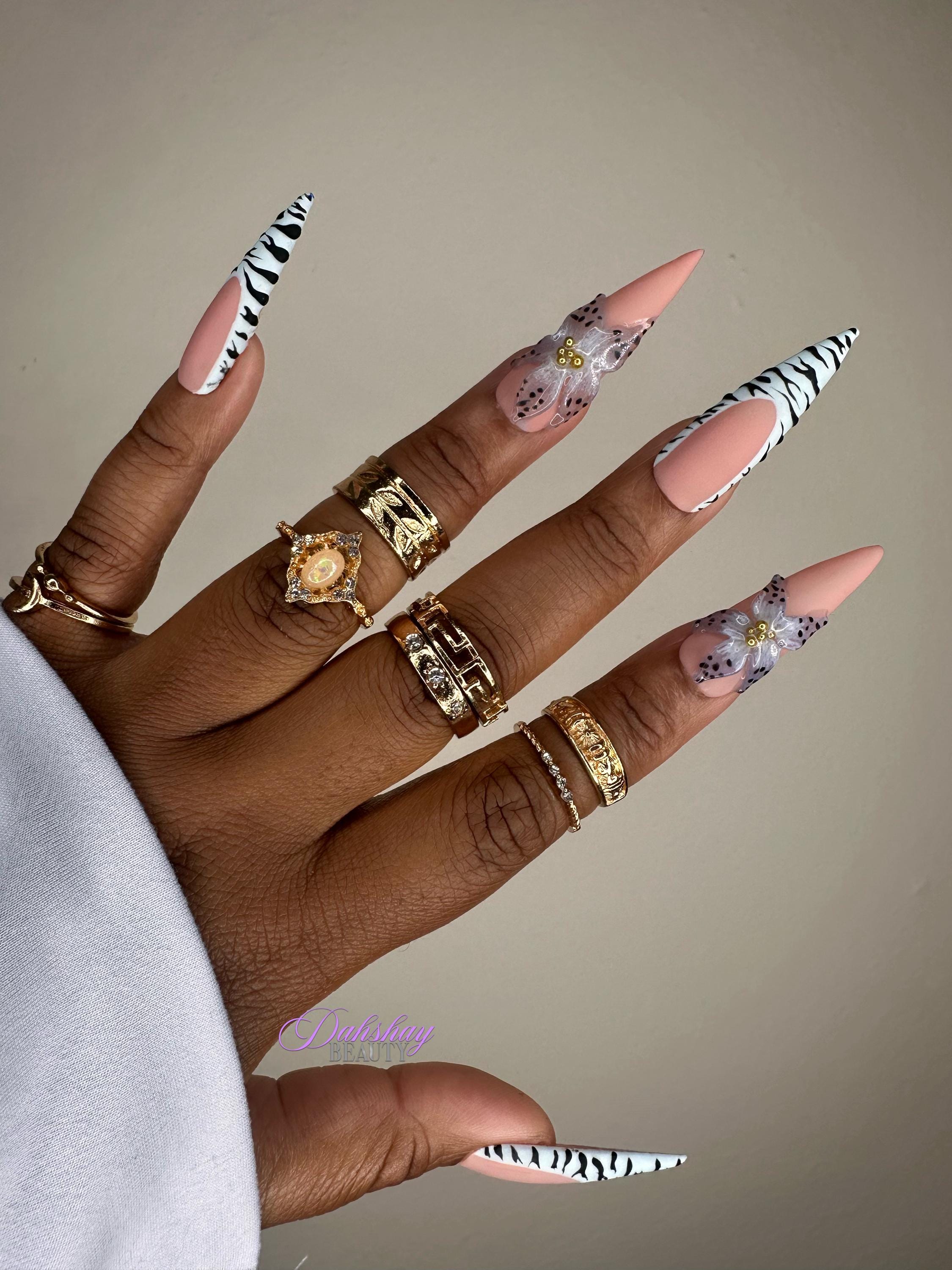 Hand with zebra print and floral nail designs on a neutral background with gold rings