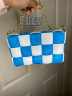 Blue and white checkered handbag with gold chain handle held by a hand against a neutral background.