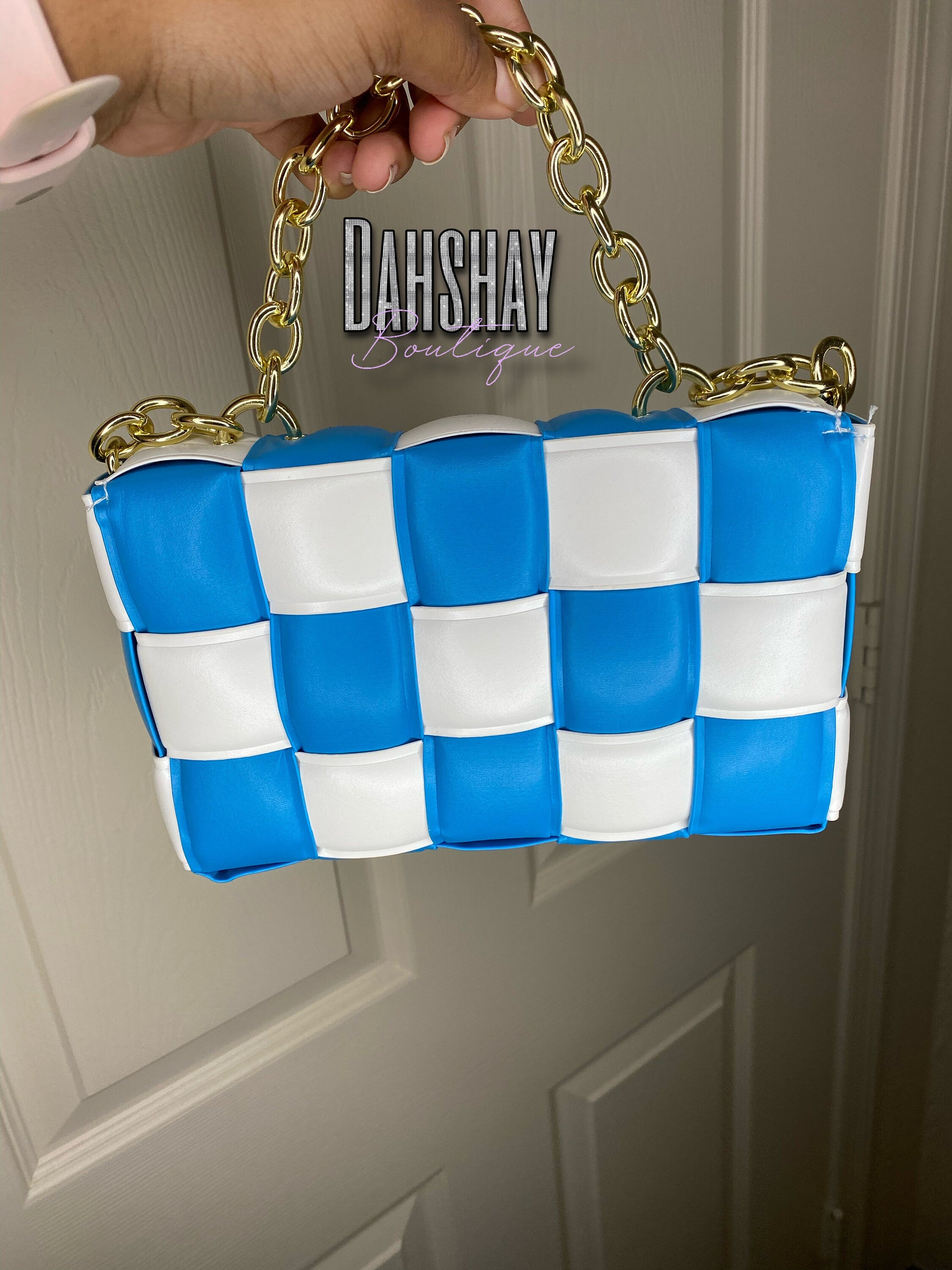 Blue and white checkered handbag with gold chain handle held by a hand against a neutral background.