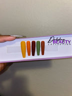 Set of false nails in various Fall colors on a display card with a purple glitter background.