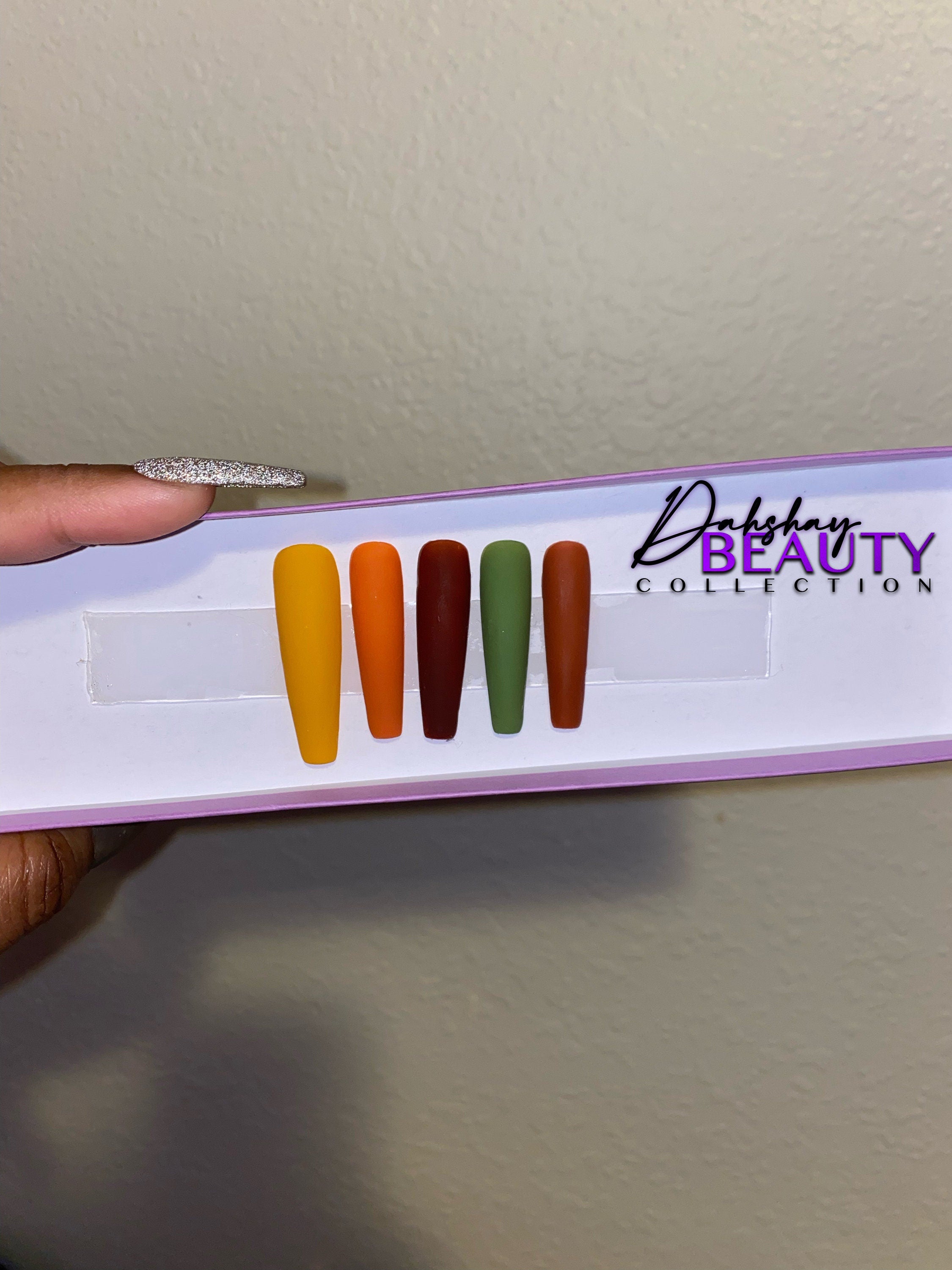 Set of false nails in various Fall colors on a display card with a purple glitter background.