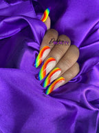Close-up of a hand with rainbow nail design on a purple fabric background, featuring the 'Dahshay Beauty Collection' brand.
