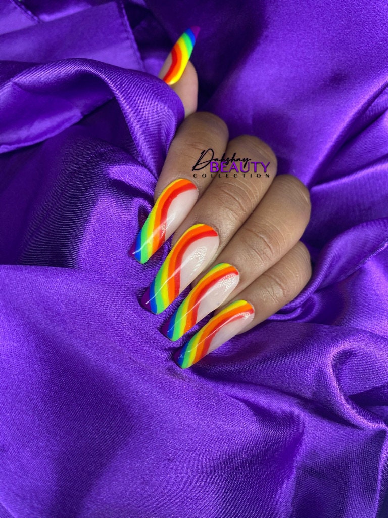 Close-up of a hand with rainbow nail design on a purple fabric background, featuring the 'Dahshay Beauty Collection' brand.