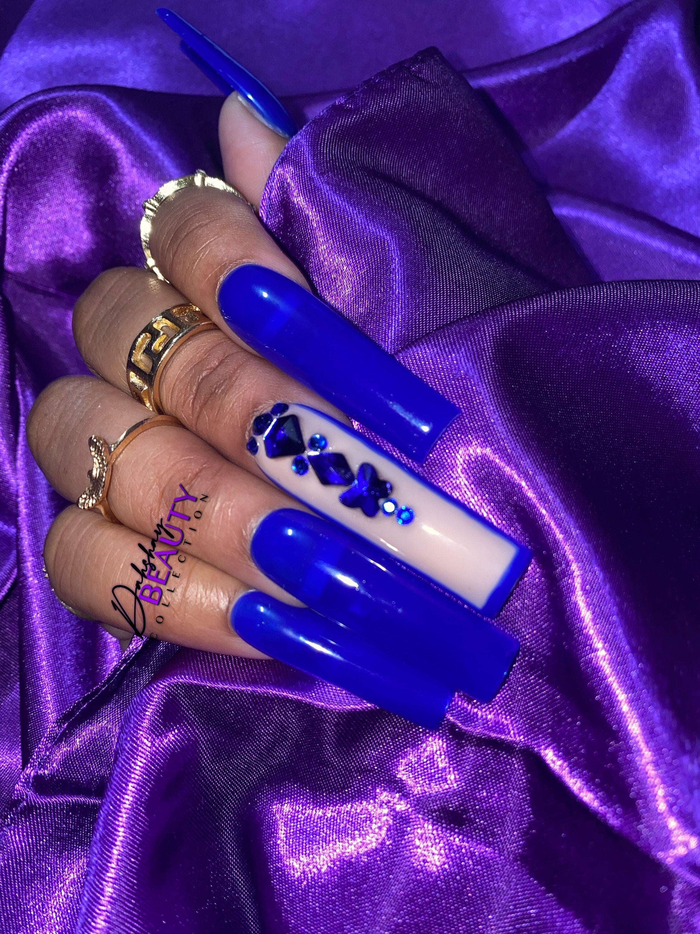 Blue nails with a rhinestone design on a purple satin background