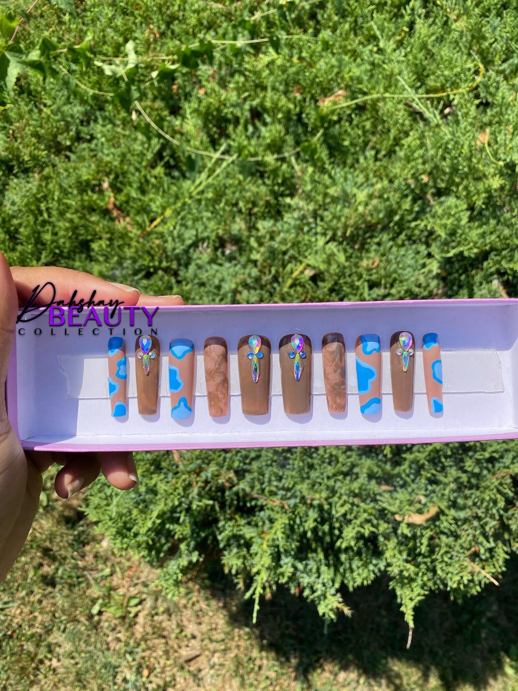 Nail art display with blue and brown designs held against a green outdoor background
