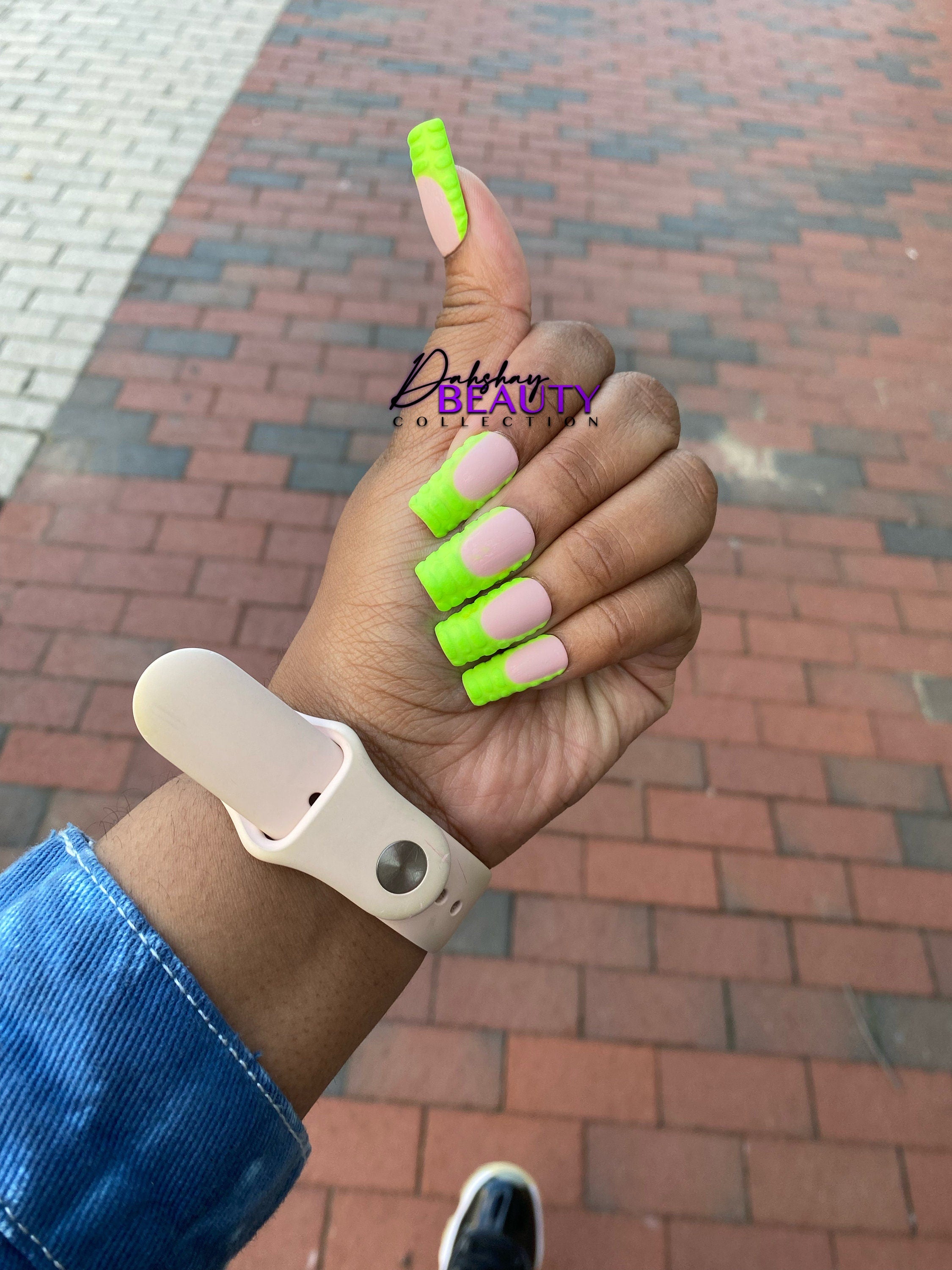 Hand with green french tip nails with 3D stripes outside on a brick pavement.