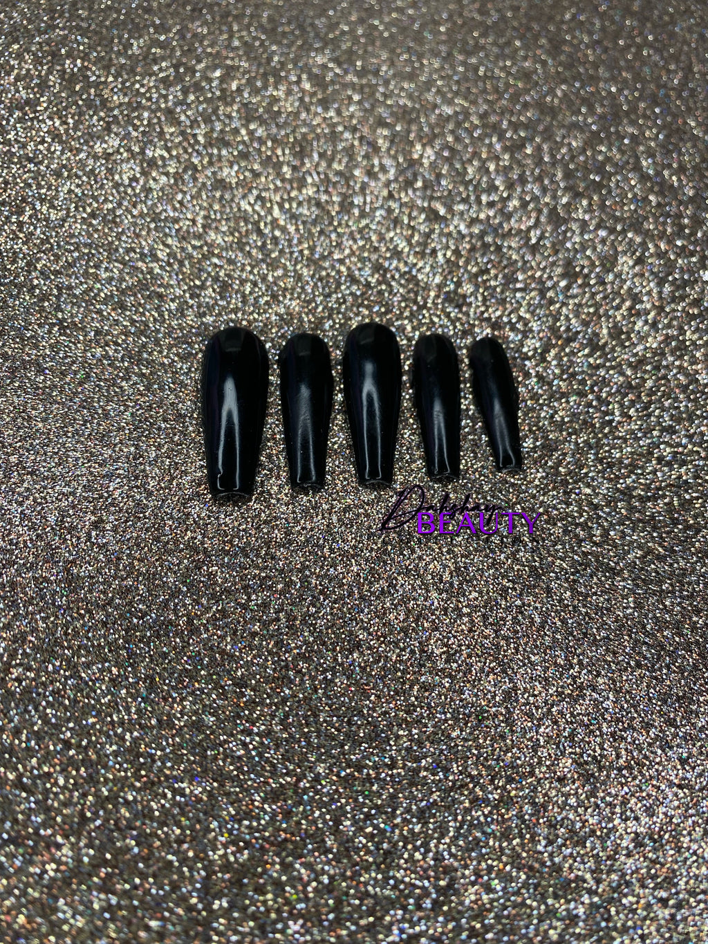 Set of black nail tips on a glittery gold background.