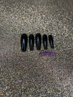 Set of black nail tips on a glittery gold background.
