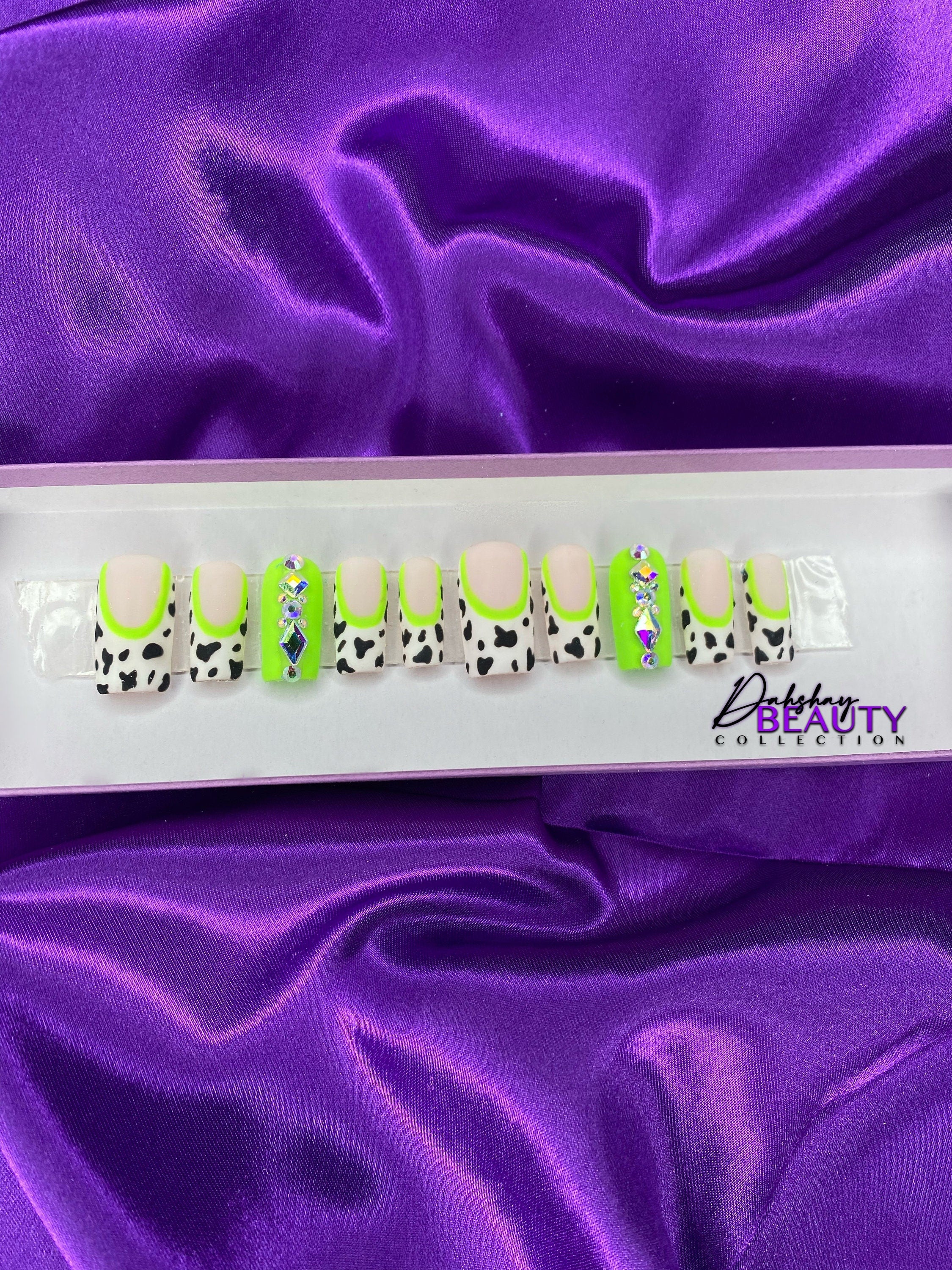 Set of false nails with cow print design on a purple satin background