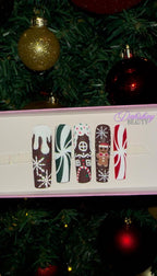 Set of Christmas gingerbread themed nail art designs on a white tray with a decorated Christmas tree in the background.