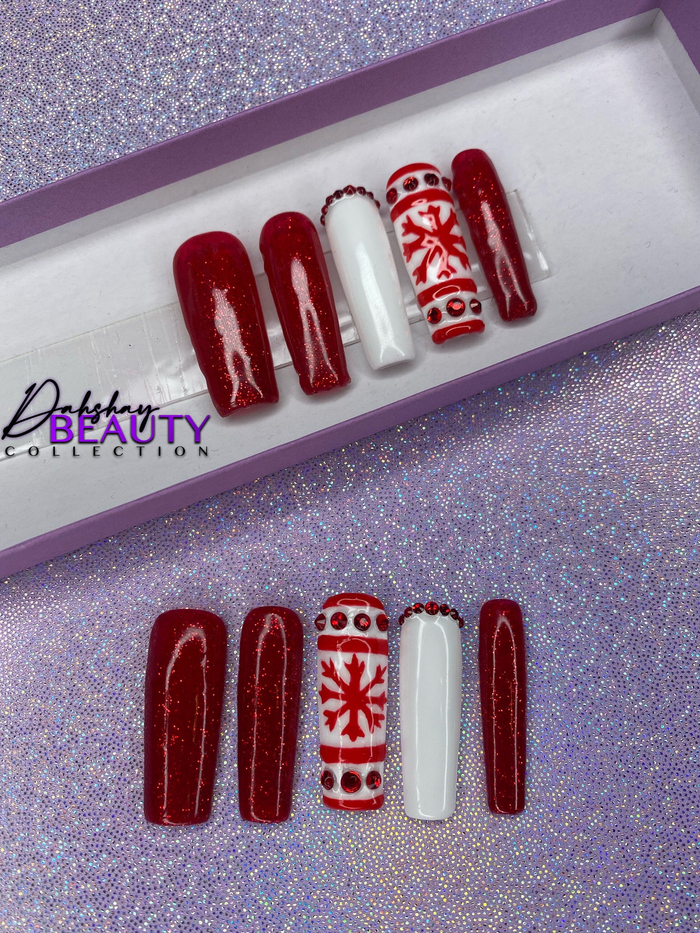 Set of Christmas red and white press on nails with red glitter and a snowflake design on a glittery purple background.