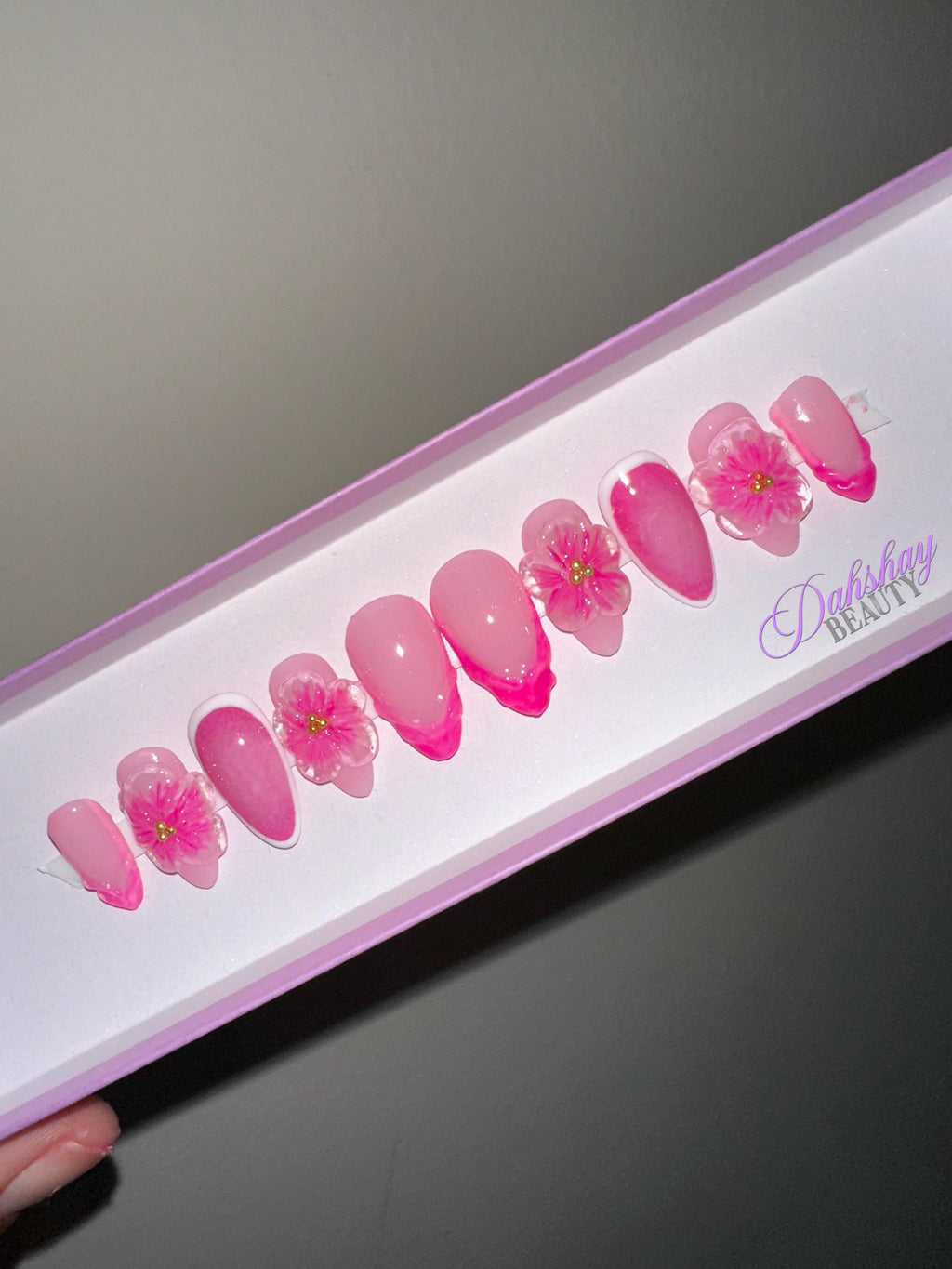Set of pink floral press on nails in a box on a plain beige background