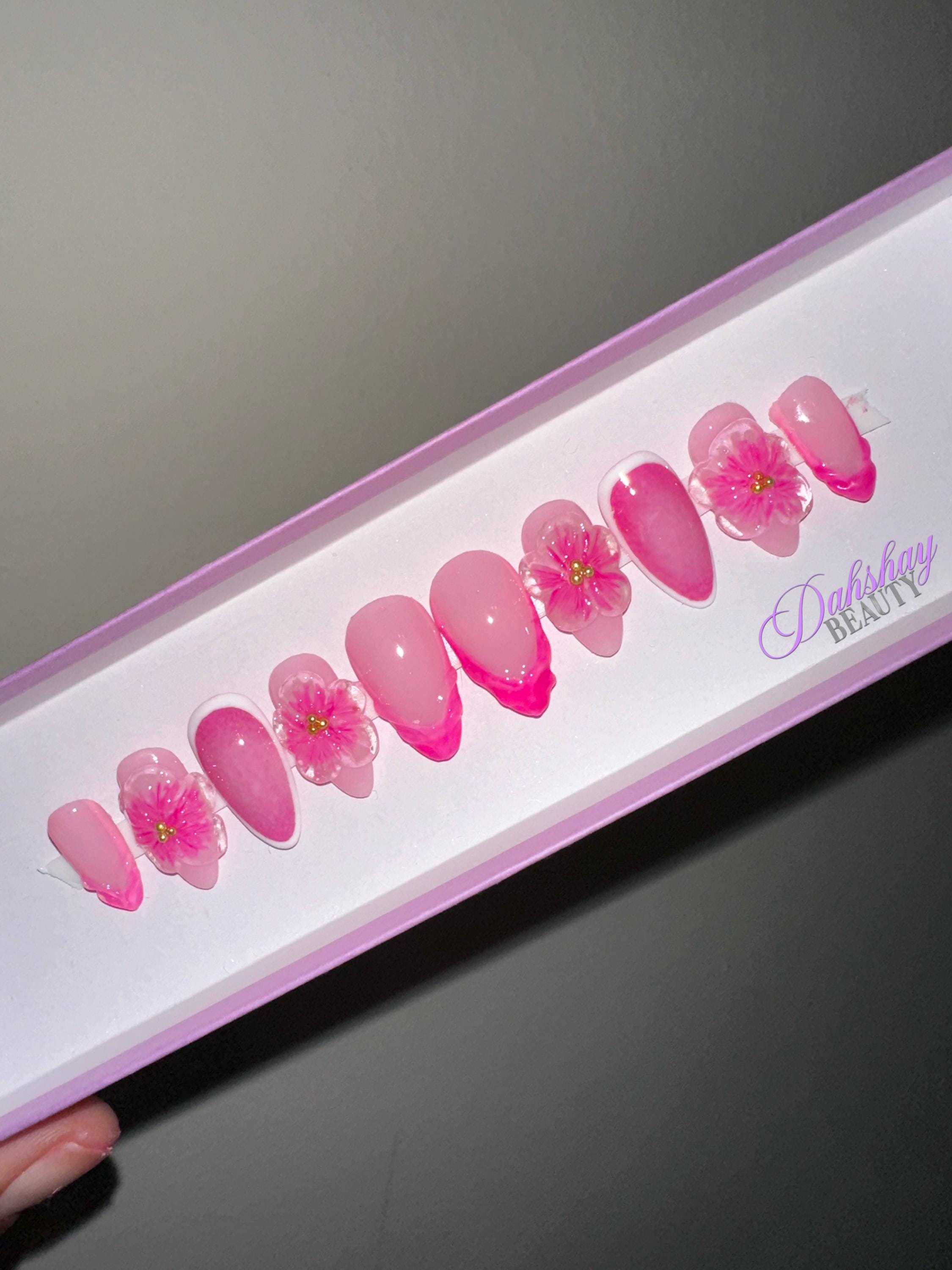 Set of pink floral press on nails in a box on a plain beige background