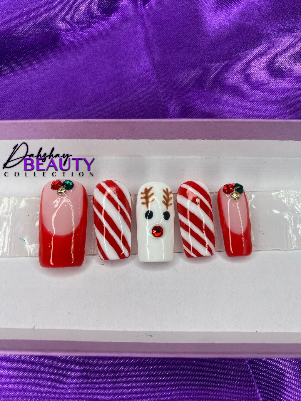 A set of Christmas nails with a reindeer, candy cane and french tip design on a purple satin background.