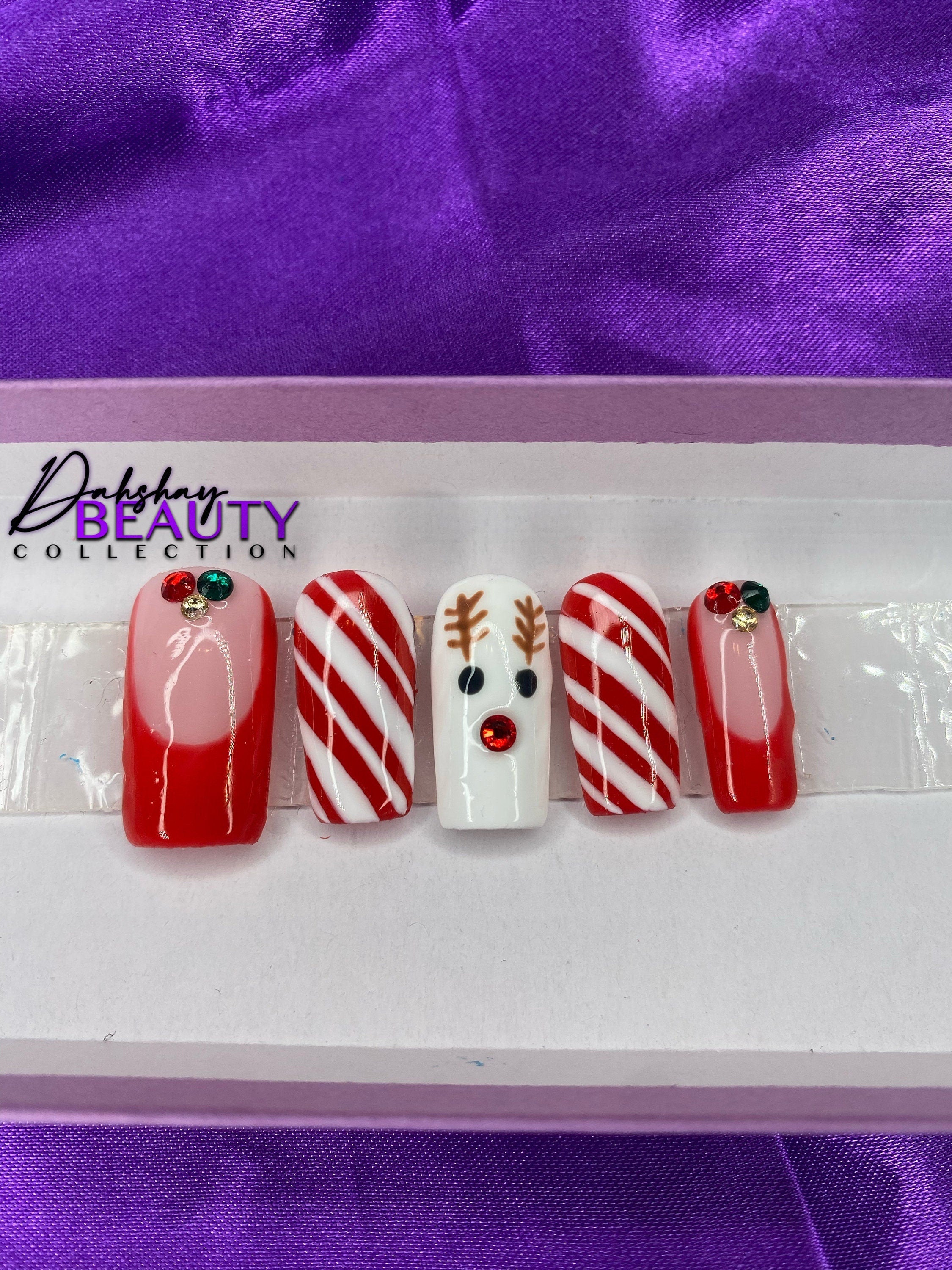 A set of Christmas nails with a reindeer, candy cane and french tip design on a purple satin background.
