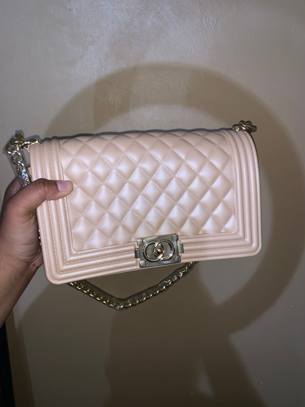 Nude quilted handbag with chain strap held by a hand against a neutral background