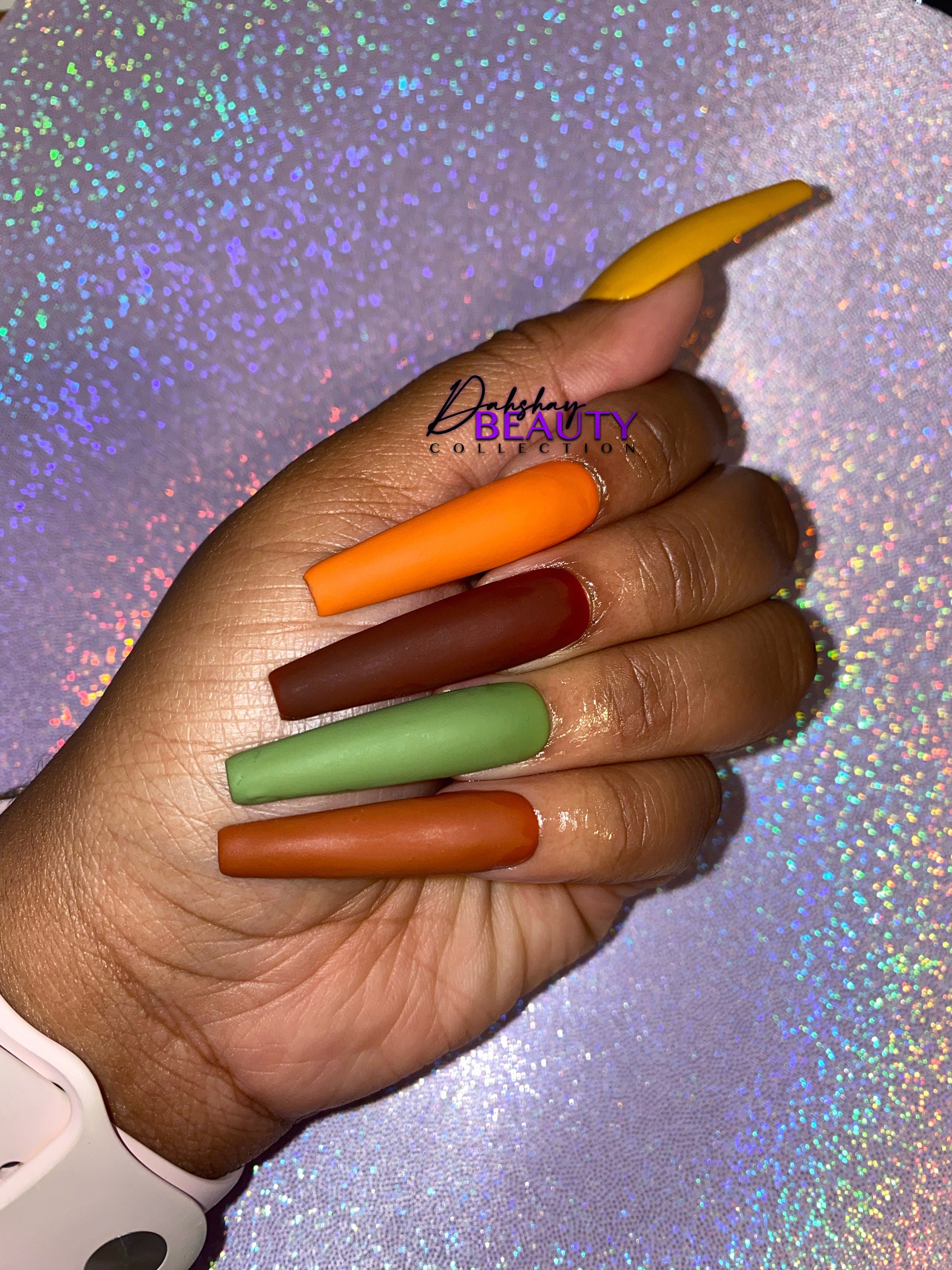 Hand with Fall multicolored nails on a glittery background.