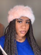 Person wearing a pink fuzzy hat with braided hair, looking directly at the camera.