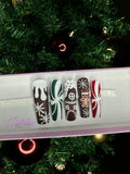 Set of Christmas gingerbread themed nail art designs on a white tray with a decorated Christmas tree in the background.