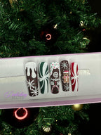 Set of Christmas gingerbread themed nail art designs on a white tray with a decorated Christmas tree in the background.