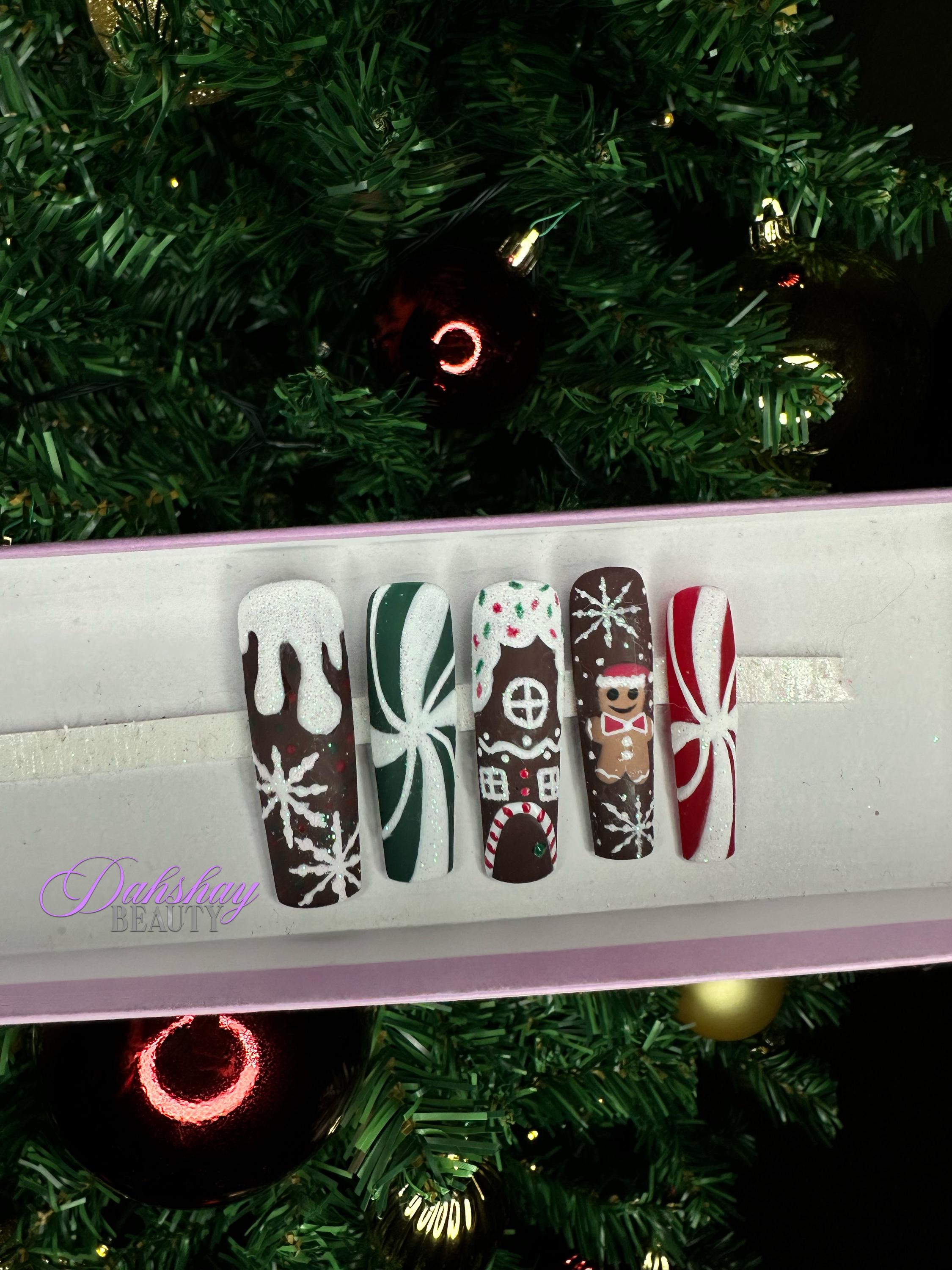 Set of Christmas gingerbread themed nail art designs on a white tray with a decorated Christmas tree in the background.