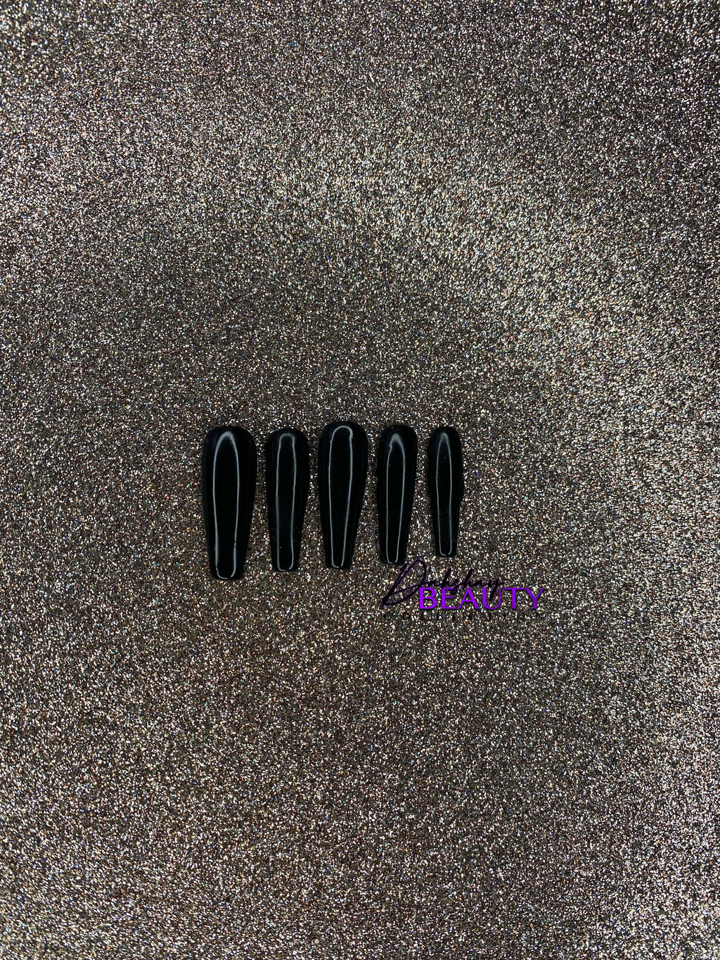 Set of black false nails on a glittery gold background.