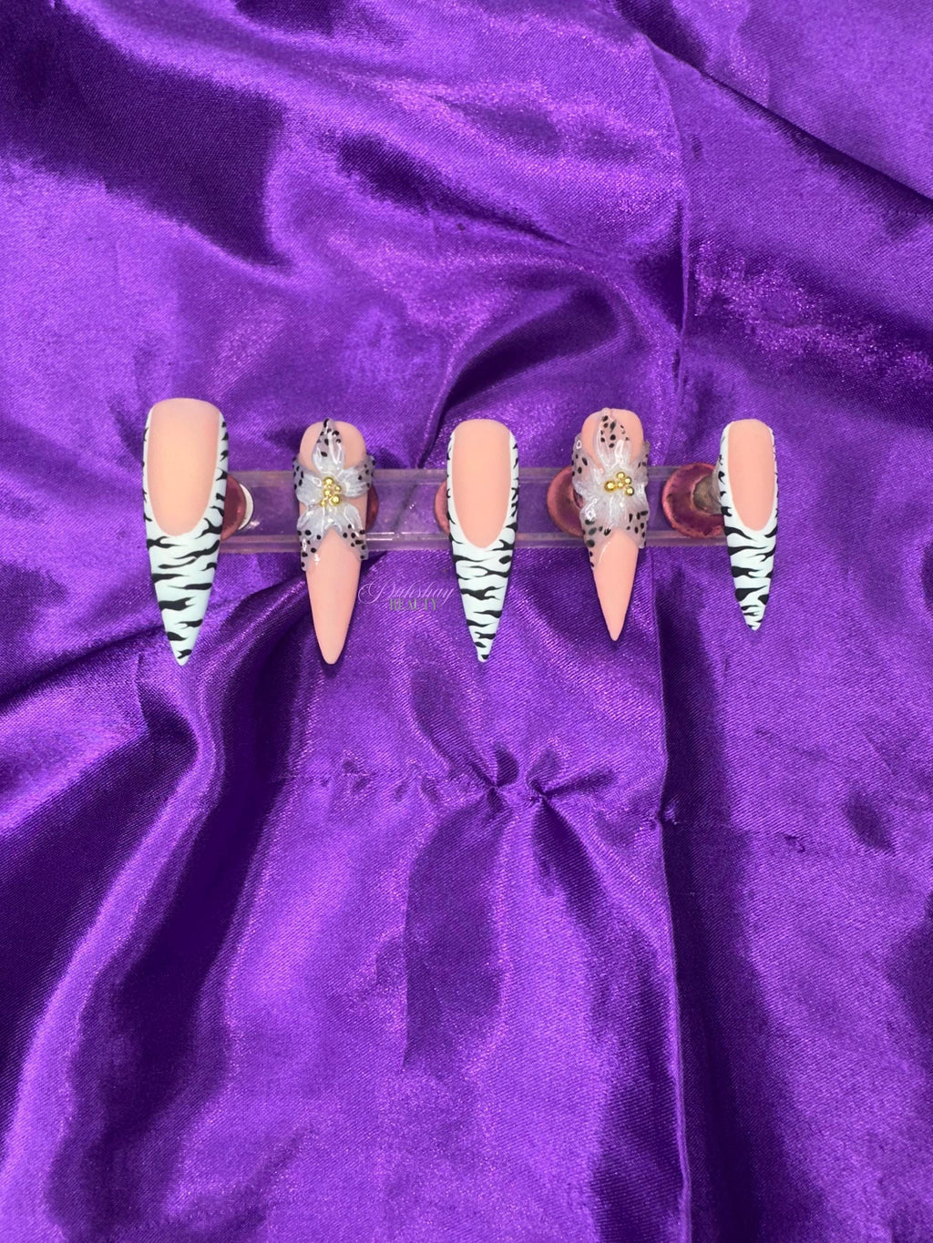 Set of false nails with zebra print design  and a floral design on a purple satin background