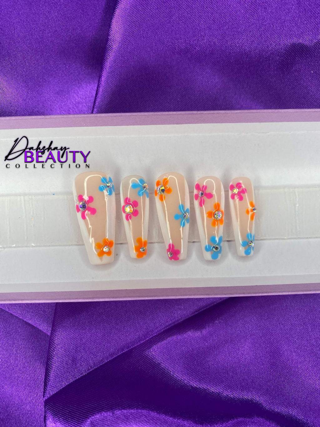 Nails with colorful floral design in a white tray on purple fabric background