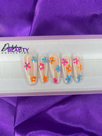 Nails with colorful floral design in a white tray on purple fabric background