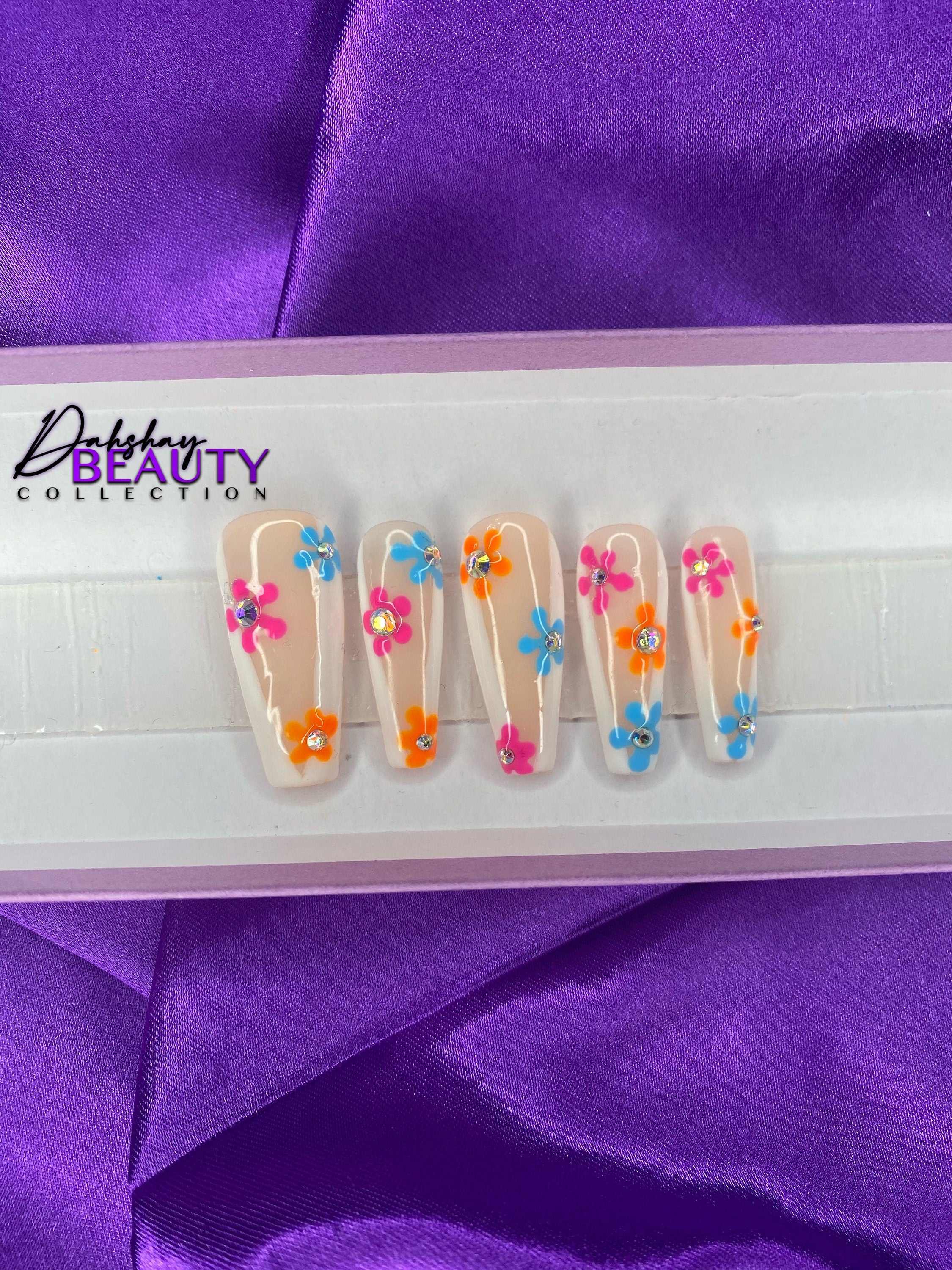 Nails with colorful floral design in a white tray on purple fabric background