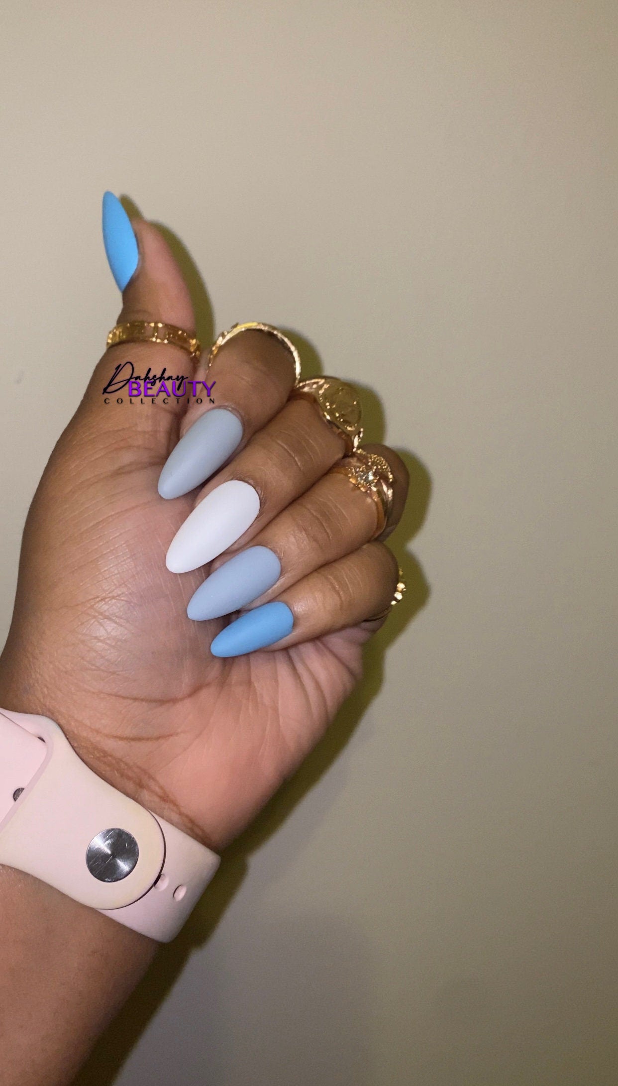 Hand with blue, grey and white nail polish wearing gold rings on a beige background