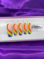 Rainbow-colored press-on nails on a white tray with 'Dahshay Beauty Collection' branding against a purple satin background.