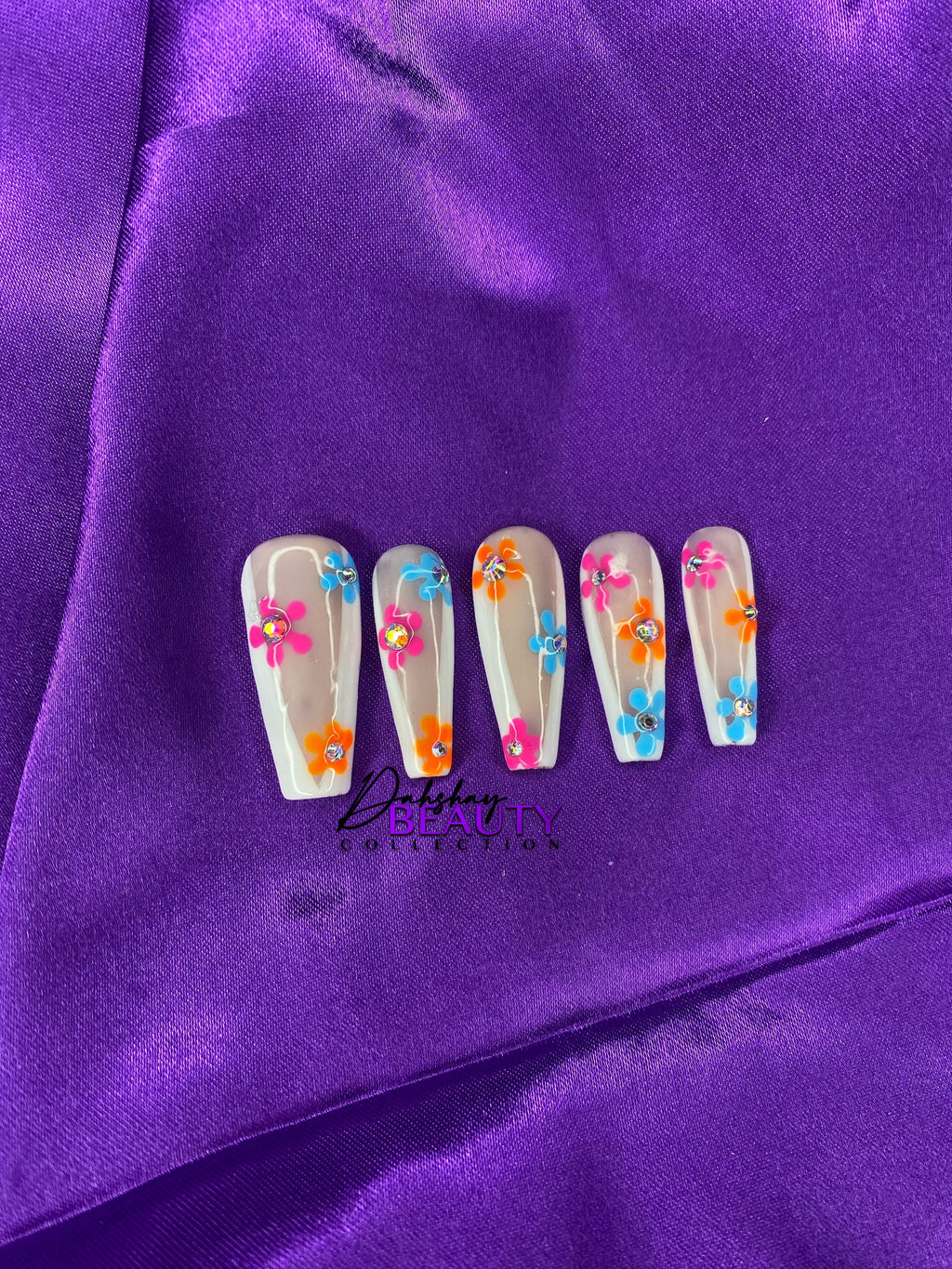 Nails with colorful floral design on purple fabric background