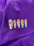 Nails with colorful floral design on purple fabric background