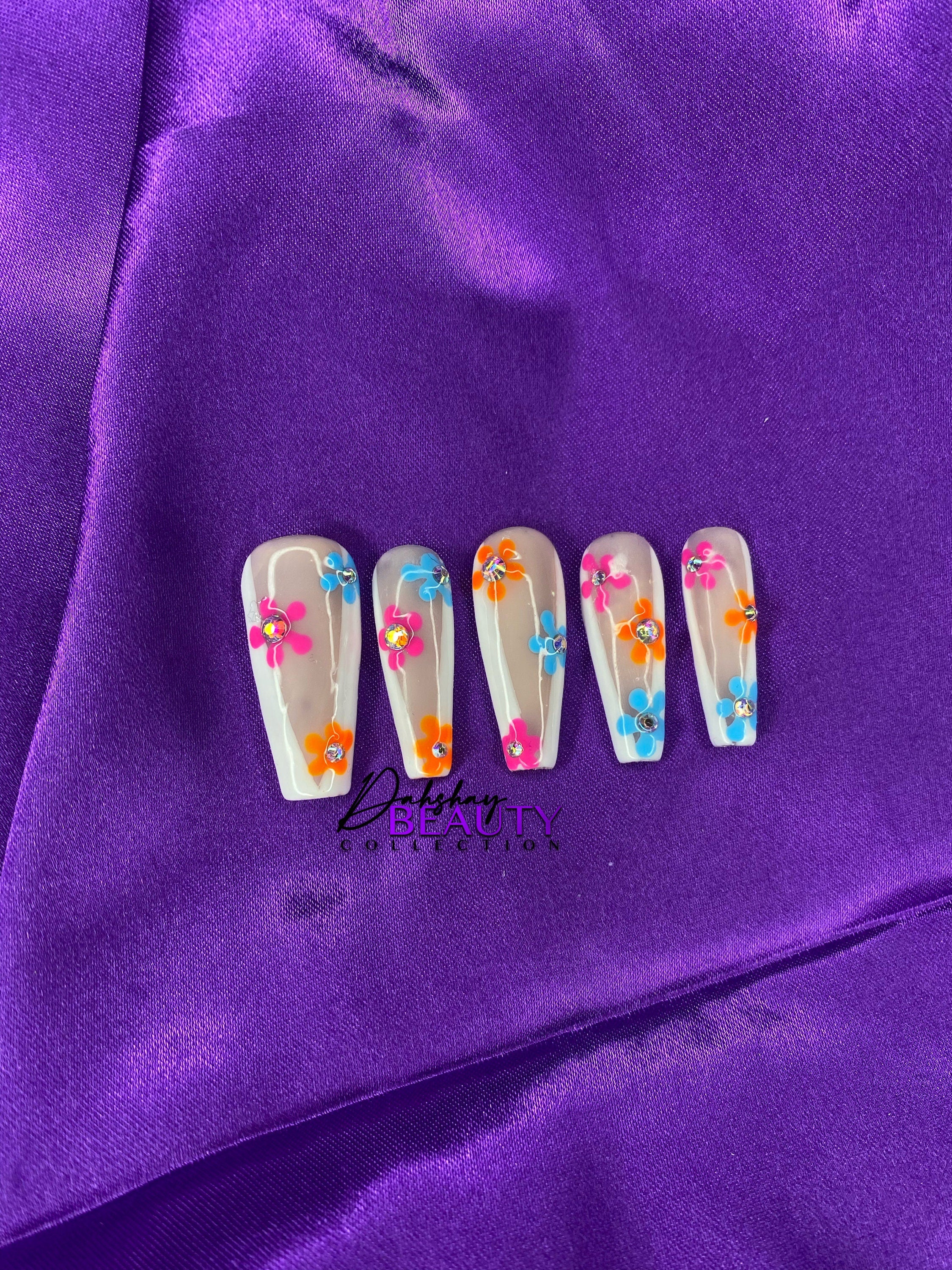 Nails with colorful floral design on purple fabric background