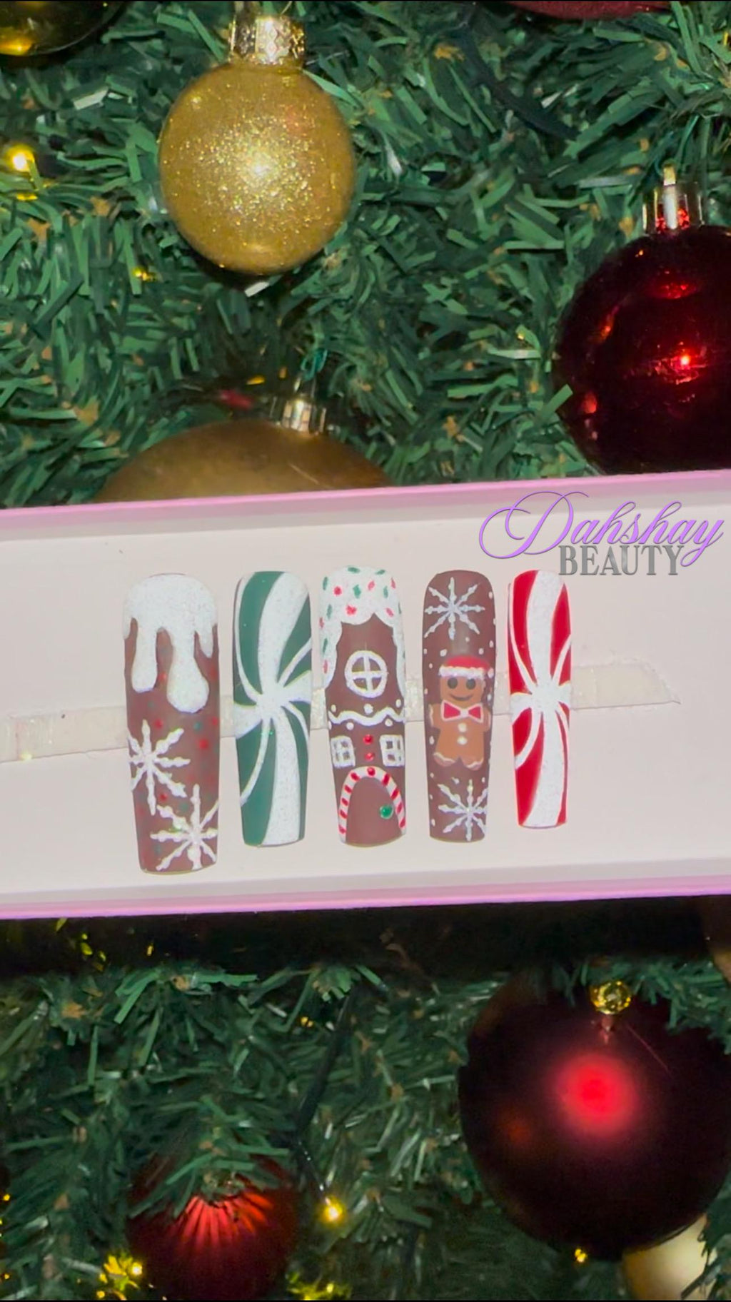 Set of Christmas gingerbread themed nail art designs on a white tray with a decorated Christmas tree in the background.