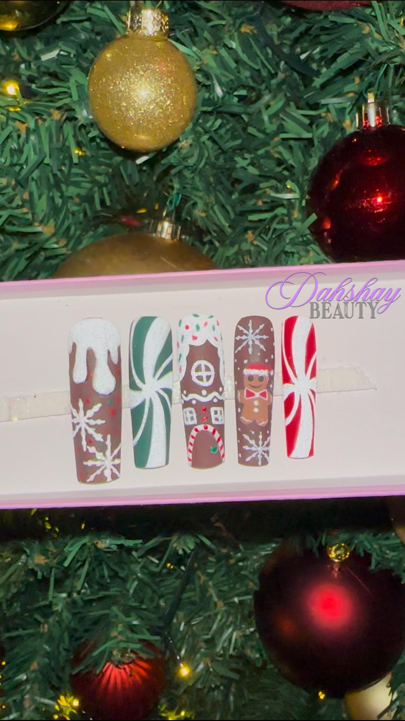 Set of Christmas gingerbread themed nail art designs on a white tray with a decorated Christmas tree in the background.