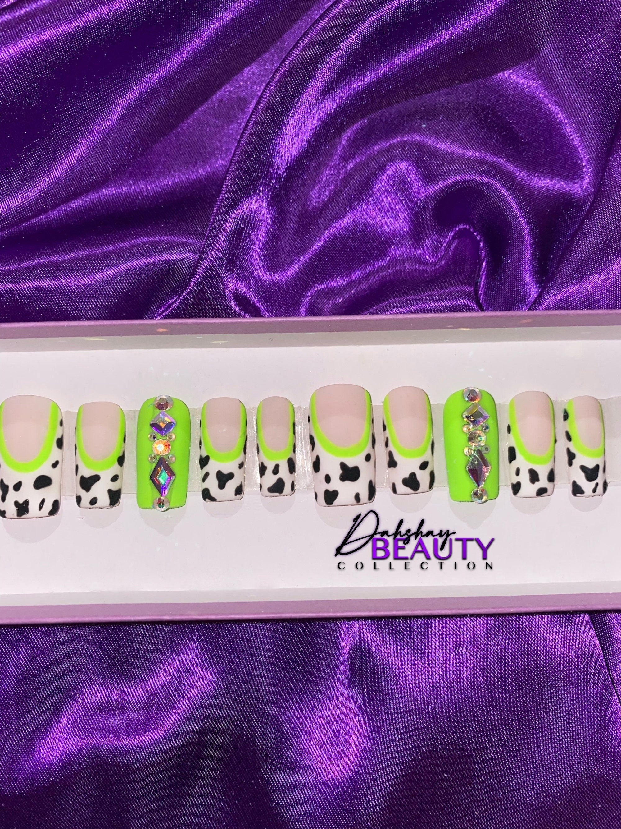 Set of false nails with green, white  abd black designs on a purple satin background