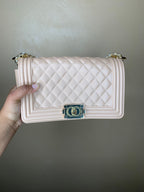 Nude quilted handbag held by a hand against a plain background