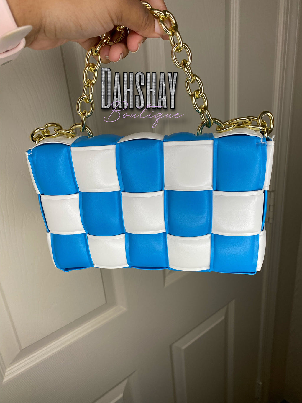 Blue and white checkered handbag with gold chain handle held by a hand against a neutral background.
